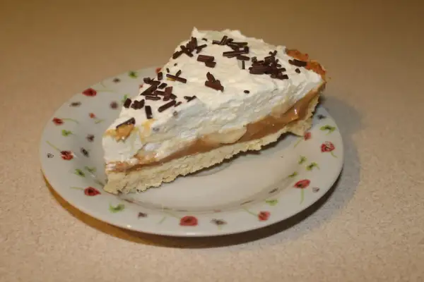 Pyszna tarta bananowa z bitą śmietaną i czekoladową posypką, podana na talerzyku w kwiatki.