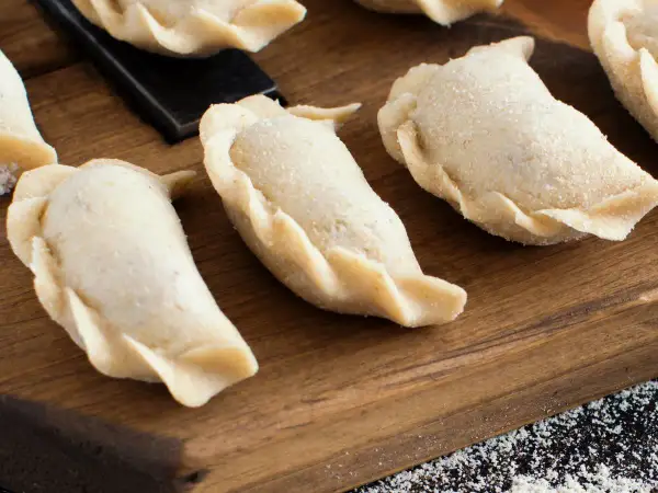 Surowe pierogi na desce. Zastanawiasz się, ile gotować pierogi, by były idealne?