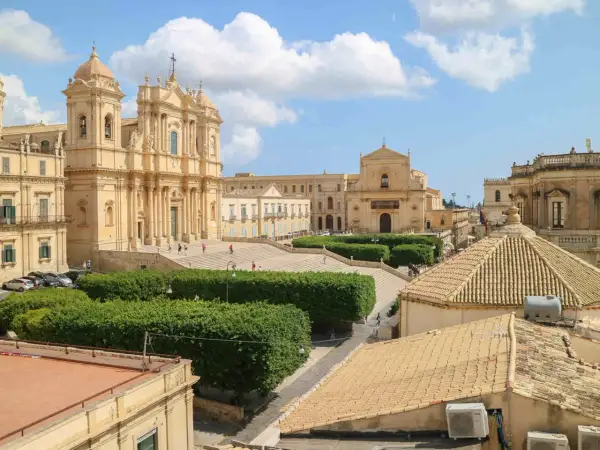 Piazza barocca con chiese imponenti e giardini curati, un esempio di città d'arte Italia sotto un cielo azzurro con nuvole bianche.