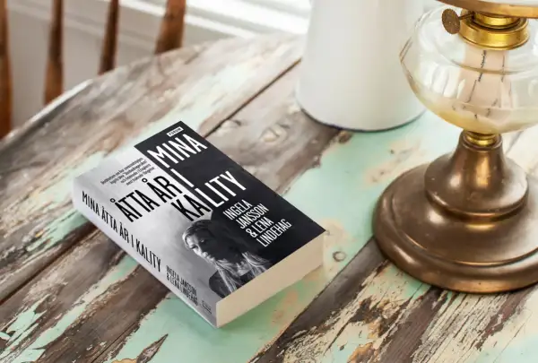 Boken "Mina åtta år i kalitet" av Ingela Jansson och Lena Lindehag ligger på ett slitet träbord.