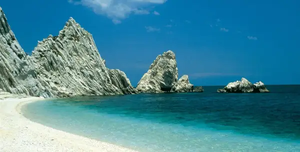 Spiaggia bianca e mare cristallino, rocce imponenti emergono dall'acqua turchese. Un angolo di paradiso nelle Marche, mare bello da cartolina.