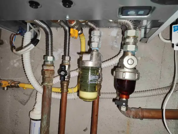 Manutenzione caldaia: pulizia filtro defangatore. Si vedono tubi, valvole e due filtri, uno con liquido giallo e uno con liquido scuro.