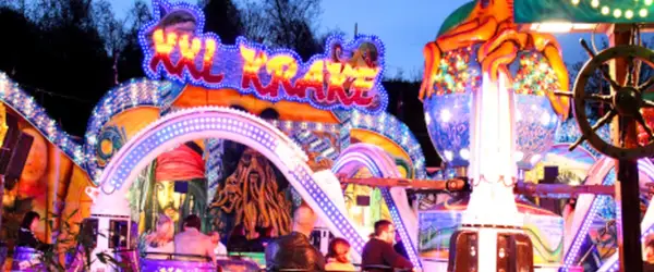 Bunte Lichter und Piratenmotive auf einer Kirmes in Berlin. Eine Achterbahn mit dem Schriftzug "Sky Krake" zieht Besucher an.
