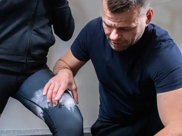 Fizjoterapeuta sprawdza kolano biegacza podczas ćwiczeń rehabilitacyjnych.