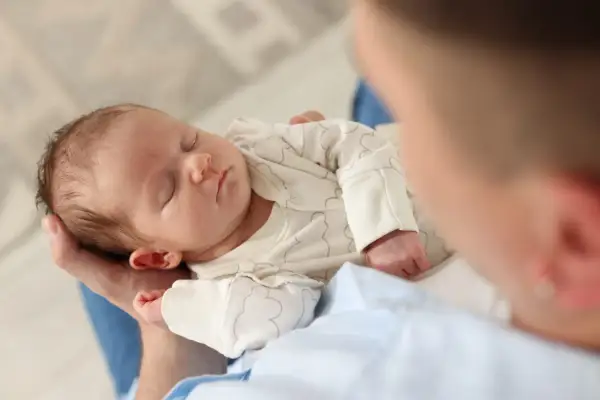 Un neonato dorme sereno tra le braccia di un genitore, cullato dal dolce rumore bianco che favorisce il sonno.