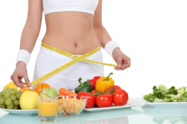 Kobieta mierzy talię centymetrem. Obok zdrowe jedzenie: owoce, warzywa, płatki. Dieta 1500 kcal efekty w zasięgu ręki!