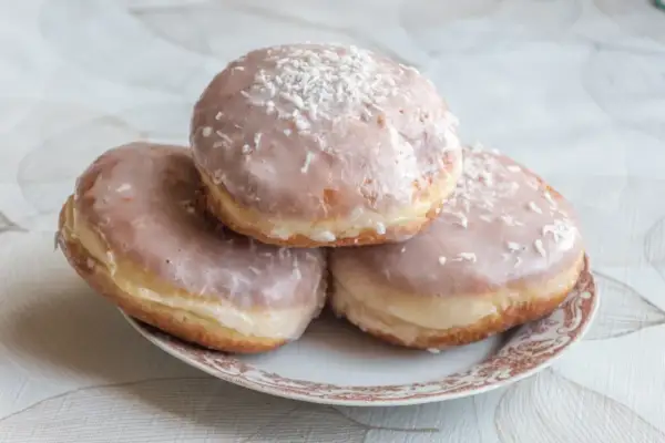Trzy pączki z lukrem do pączków i wiórkami kokosowymi na talerzyku.