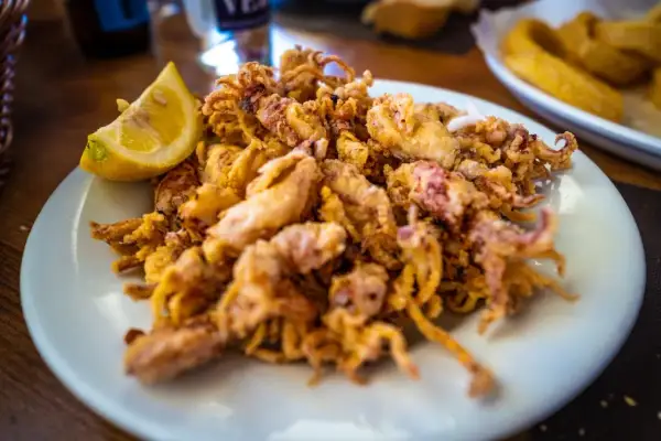 Un plato de puntillas de calamar fritas, doradas y crujientes, con un gajo de limón.