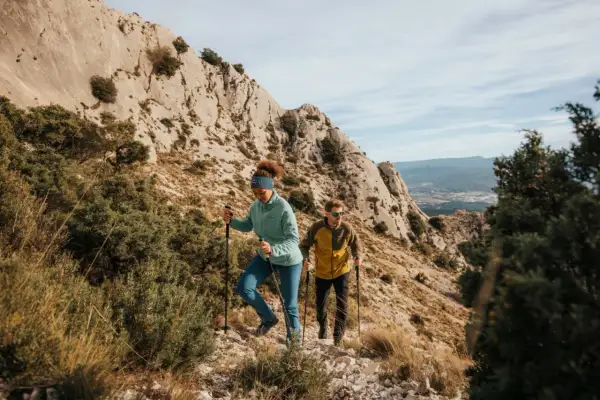 Deux randonneurs débutants progressent sur un sentier rocailleux, bâtons en main, sous un ciel bleu.