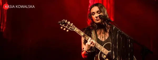 Kasia Kowalska na scenie, grając na gitarze i śpiewając. Jej utwory poruszają serca publiczności.