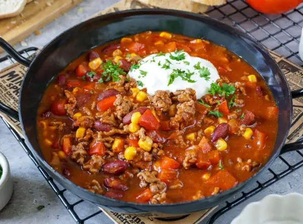 Herzhaftes Chili con Carne Rezept mit Hackfleisch, Kidneybohnen, Mais und Paprika, garniert mit einem Klecks Sour Cream und Petersilie.