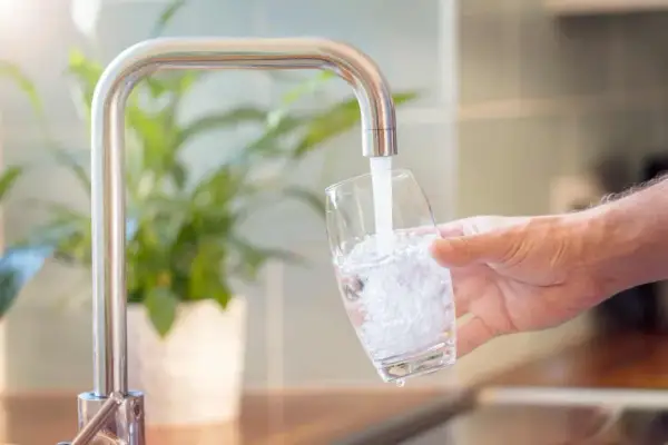 Un robinet verse de l'eau dans un verre, montrant comment obtenir de l'eau filtrée pour une boisson saine.