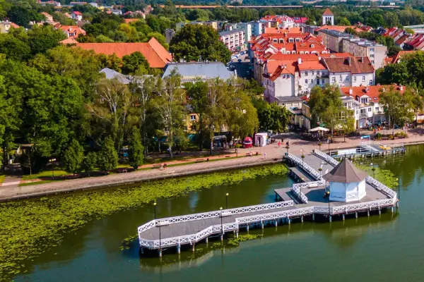 Malownicza trasa w Ostródzie nad jeziorem z promenadą i altanką. W tle zabudowa miejska i zieleń.