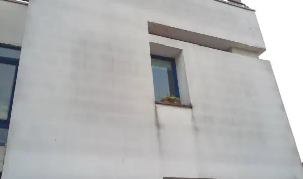Facciata di un edificio con cappotto termico che mostra segni di muffa e macchie scure sotto la finestra.