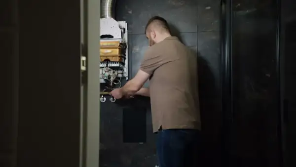 Mężczyzna naprawia piecyk gazowy Junkers, z którego kapie woda.