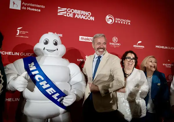 Bibendum, el muñeco Michelin, sonríe junto a autoridades en un evento que celebra la gastronomía de Huesca, destacando la **estrella Michelin Huesca**.