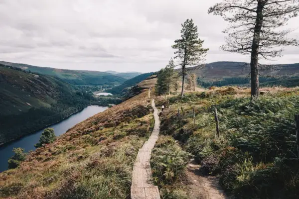 Sentier en bois serpentant sur une colline verdoyante, dominant un lac bleu profond et des montagnes dans le **gr irlande**.