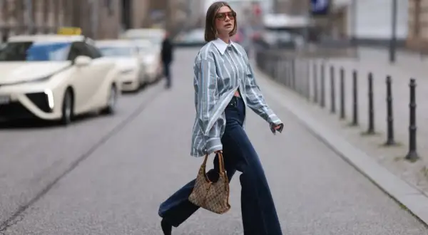 Kobieta w luźnej, pasiastym koszuli i dżinsach pokazuje, jak nosić koszule w miejskim stylu. Torba na ramię dodaje elegancji.
