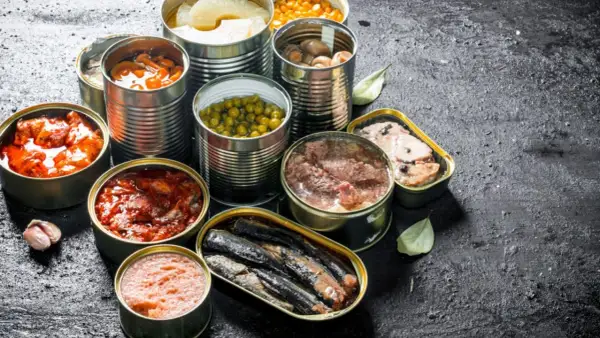 Variedad de latas abiertas con comida supervivencia: guisantes, champiñones, sardinas, carne y más.