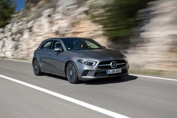 Une Mercedes-Benz Classe A grise roule sur une route de campagne, le paysage flou par la vitesse. Son moteur classe a offre une conduite dynamique.