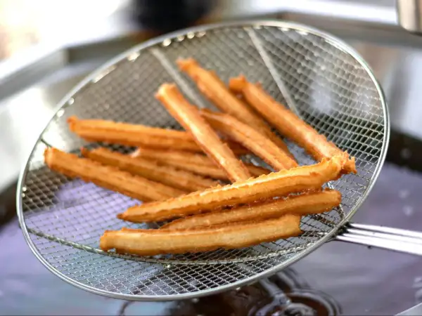 Złociste churros na sicie, właśnie wyjęte z gorącego oleju. Pytasz churros co to? To pyszny, smażony przysmak!