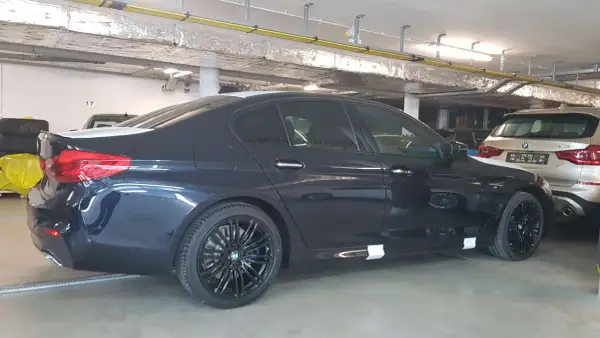 Ciemnogranatowe BMW 520d xDrive z czarnymi felgami stoi w garażu.