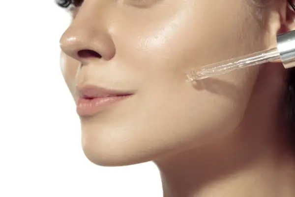 Eine Pipette gibt ein Serum auf die Wange einer Frau. Ein Tropfen mit Glykolsäure deutsch für strahlende Haut.