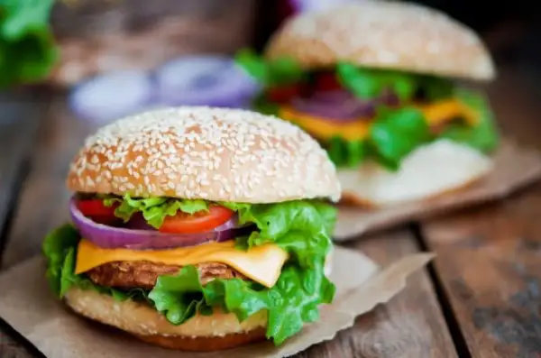 Dwa soczyste burgery z domowym fast foodem, pełne świeżych warzyw i sera, na drewnianym stole.