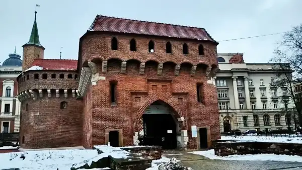 Imponujący barbakan kraków z cegły, z charakterystycznymi łukami i blankami, otoczony zimowym krajobrazem.