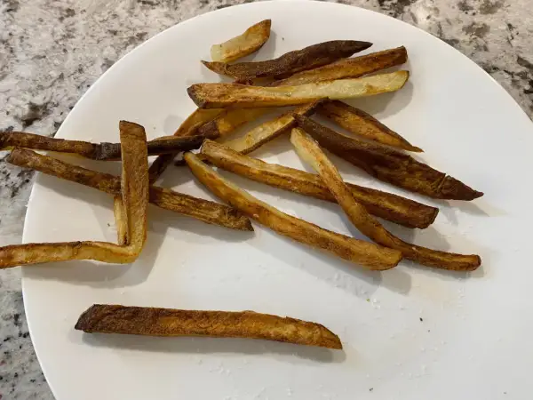 En tallrik med krispiga pommes frites, perfekt tillagade i airfryer. Saltkorn glittrar på de gyllene pommes.