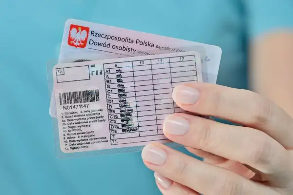 Dłoń trzyma polskie prawo jazdy z kategorią B, obok dowód osobisty.