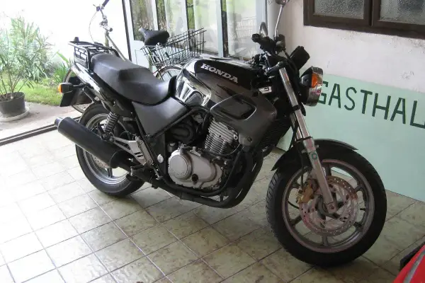 Czarny motocykl Honda z widocznym silnikiem i wydechem, gotowy do jazdy. Obok stoi rower.