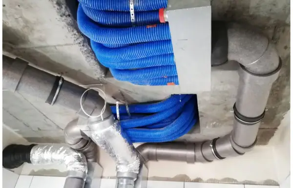 Instalacja rekuperacji w starym domu. Niebieskie przewody wentylacyjne i szare rury tworzą skomplikowany system pod sufitem.