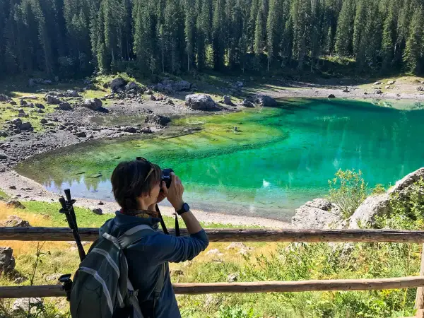 Donna con zaino e macchina fotografica cattura la bellezza del Lago di Carezza, un luogo imperdibile tra le meraviglie del Trentino Alto Adige cosa vedere.