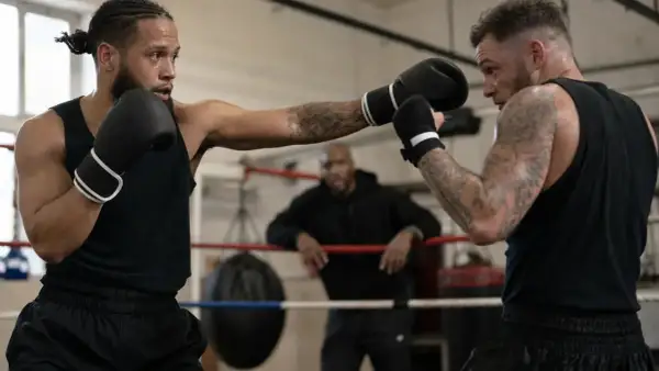 Two boxers spar in a ring, one throwing a jab, demonstrating how to counter punch. A coach watches from the background.