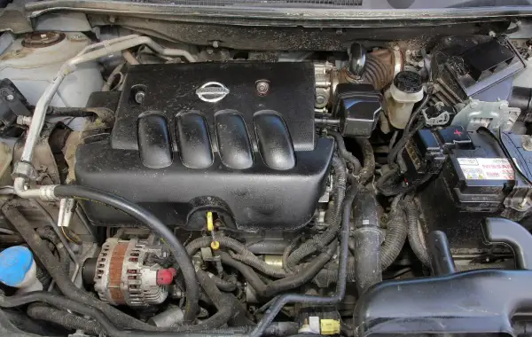 Silnik Nissan Qashqai J10, widok z góry. Czarna pokrywa silnika z logo Nissan, alternator, akumulator i przewody.