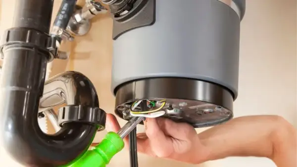 A person is working on a garbage disposal that is not working, connecting wires with a screwdriver.
