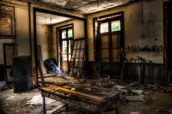 Intérieur d'un lieu abandonné en France. Un vieux bureau en bois trône au milieu des débris, sous des ampoules nues.