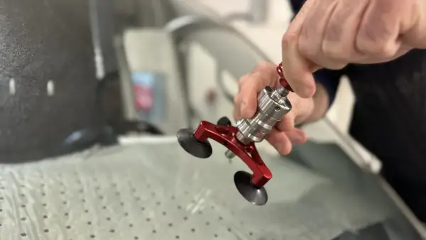 En person använder ett verktyg för att laga en spricka i en bilruta. Verktyget har sugproppar och en metallkonstruktion.