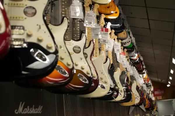 Rząd gitar elektrycznych w sklepie. Widać różne kolory i modele, w tym pierwsza gitara elektryczna z pięknym wykończeniem.