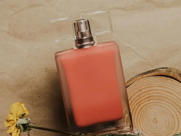 Perfumy Lancome Oui w koralowym odcieniu, obok suszonej róży i plastra drewna.
