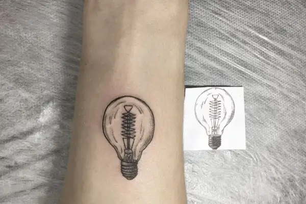 Nowy tatuaż żarówka na skórze, obok szkicu. Symbol pomysłu i światła.