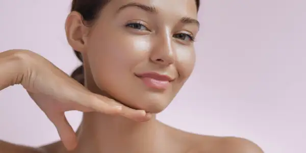 Strahlendes Gesicht einer Frau, die ihr Kinn berührt. Die Haut wirkt glatt und jugendlich, ein Zeichen für die positive retinol wirkung.