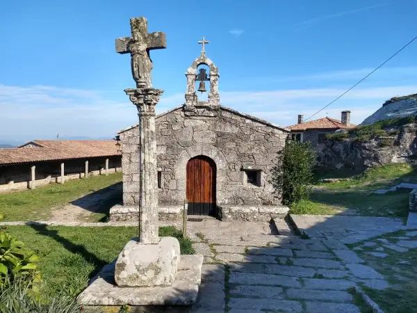 Crucero y ermita de piedra en el Castro de Santa Trega, bajo un cielo azul.