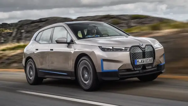 Złoty BMW iX jedzie po drodze, otoczony skalistym krajobrazem.