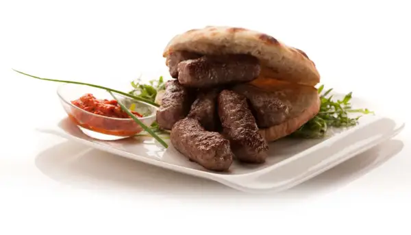 En tallrik med balkan mat: saftiga köttfärsrullar i pitabröd, serverade med en röd röra och grönsaker.