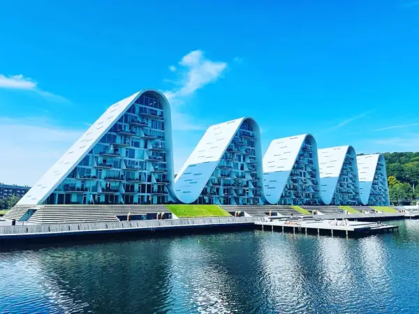 Vågformade byggnader vid vattnet i Vejle, Danmark. Moderna lägenheter med glasfasader och balkonger.