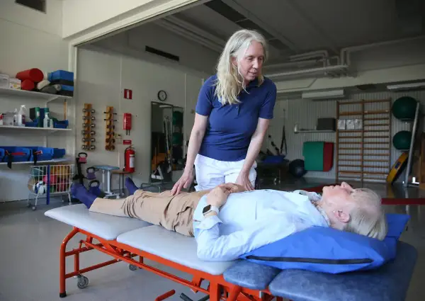 Fysioterapeut undersöker en patient som ligger på en brits. Patienten verkar vara fixerad bebis i sin position, redo för behandling.