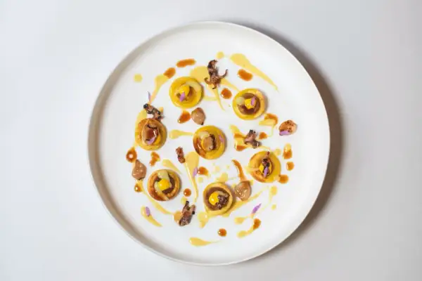 Piccolo capolavoro culinario: tartellette dorate con ripieno giallo, guarnite con calamari croccanti e fiori viola. Un'opera d'arte degna di un ristorante con massimo stelle Michelin.