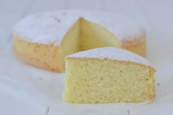 Una soffice torta con farina di riso, spolverata di zucchero a velo, con una fetta tagliata.